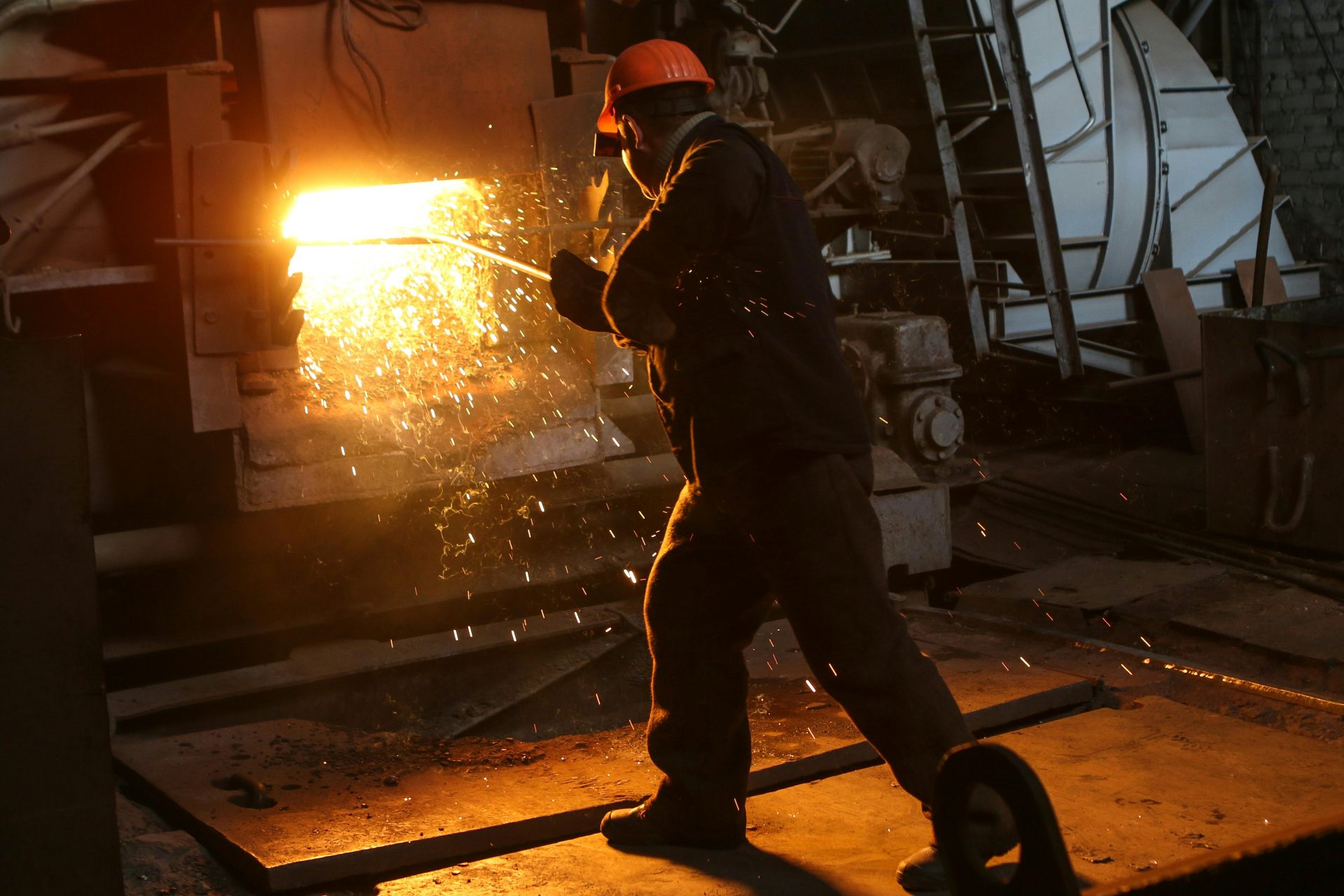 Ein Arbeiter in Schutzkleidung schweißt Metall in einer Industrieanlage, wobei Funken sprühen.