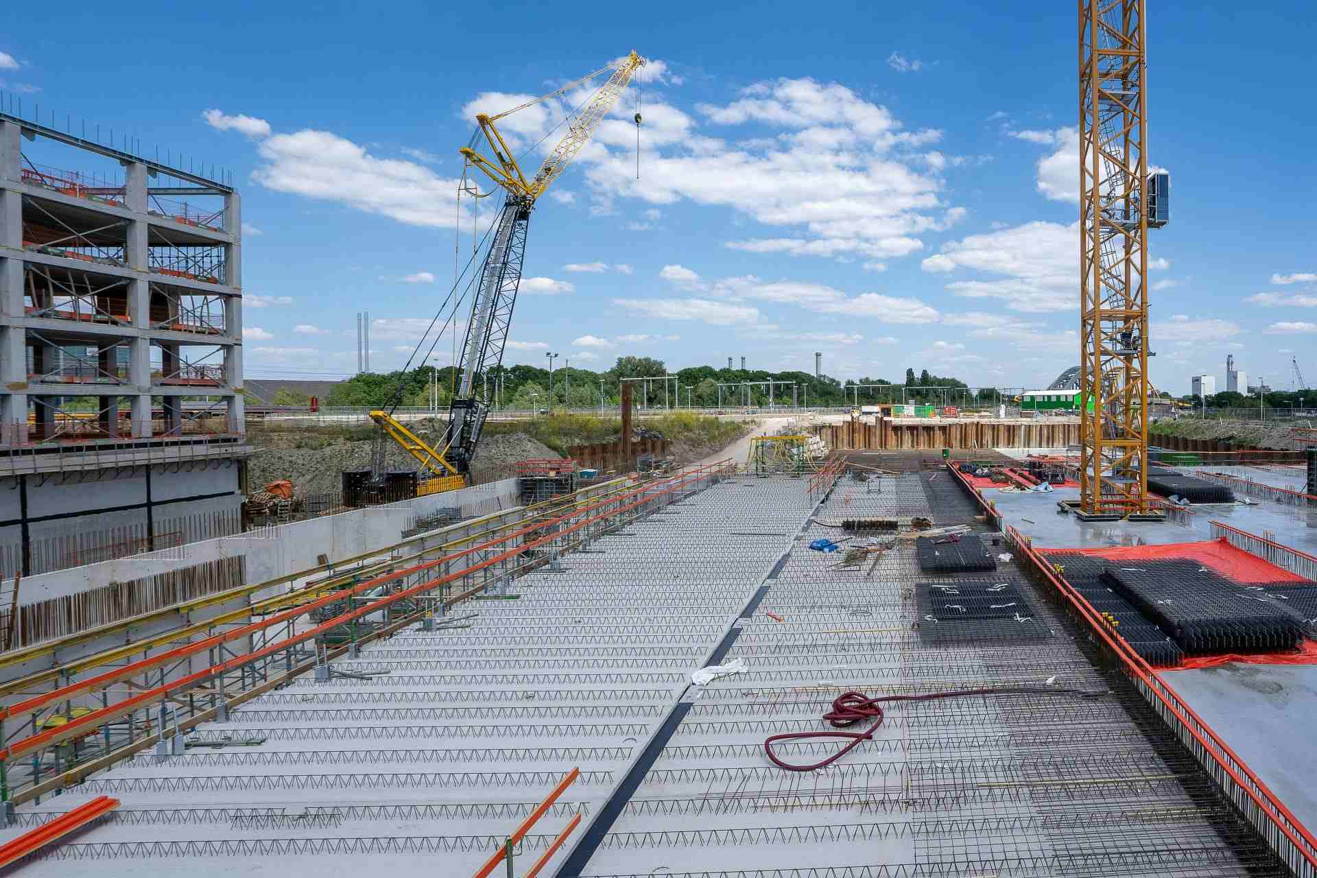 Blick auf eine geschäftige Baustelle mit Kränen und Gebäudestrukturen unter klarem Himmel.